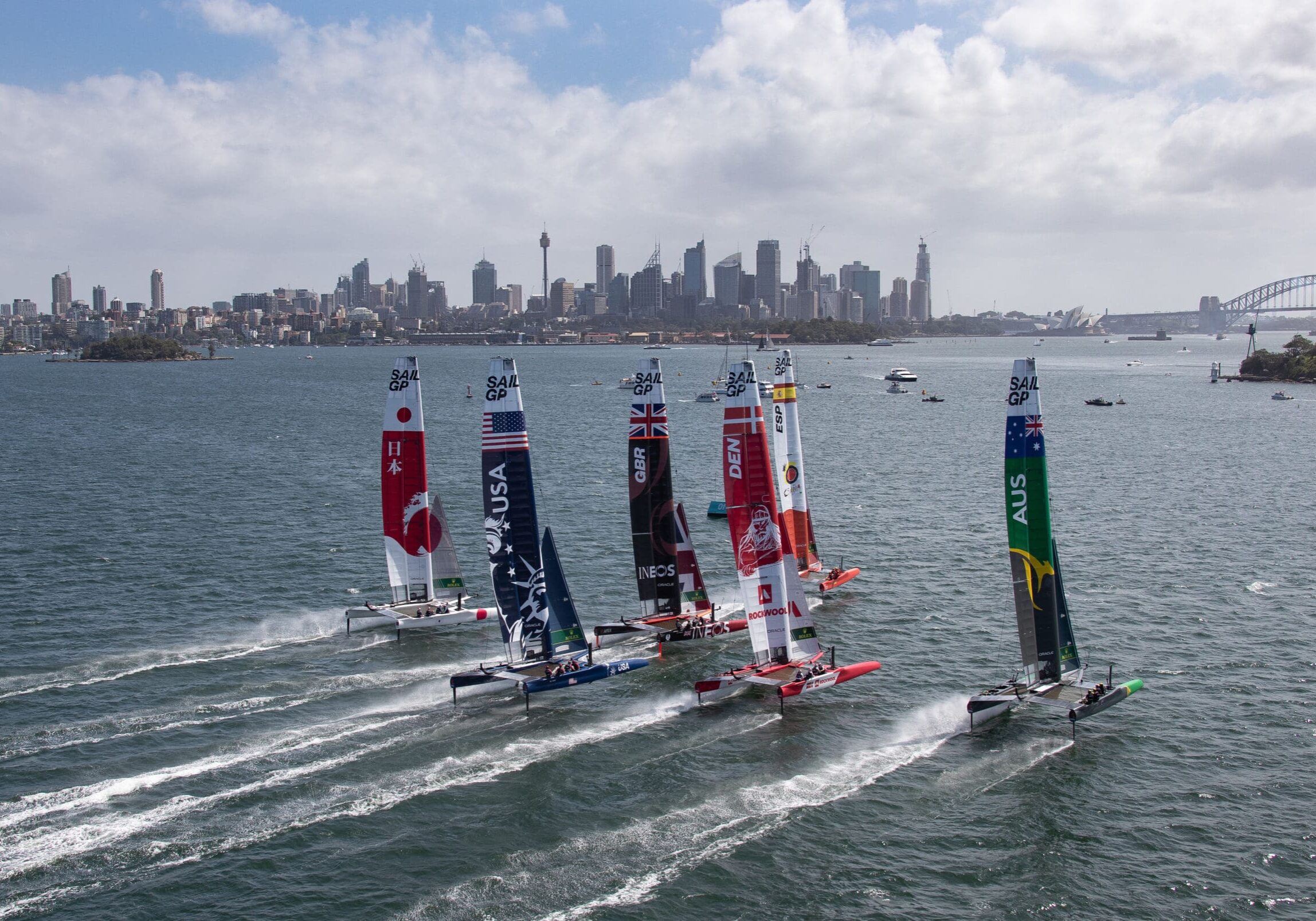 Aerial view of the fleet racing side by side with Sydney Harbour Bridge in the distance, during practice ahead of the Sydney SailGP, Event 1 Season 2 in Sydney Harbour, Sydney, Australia. 27 February 2020. Photo: David Gray for SailGP. Handout image supplied by SailGP